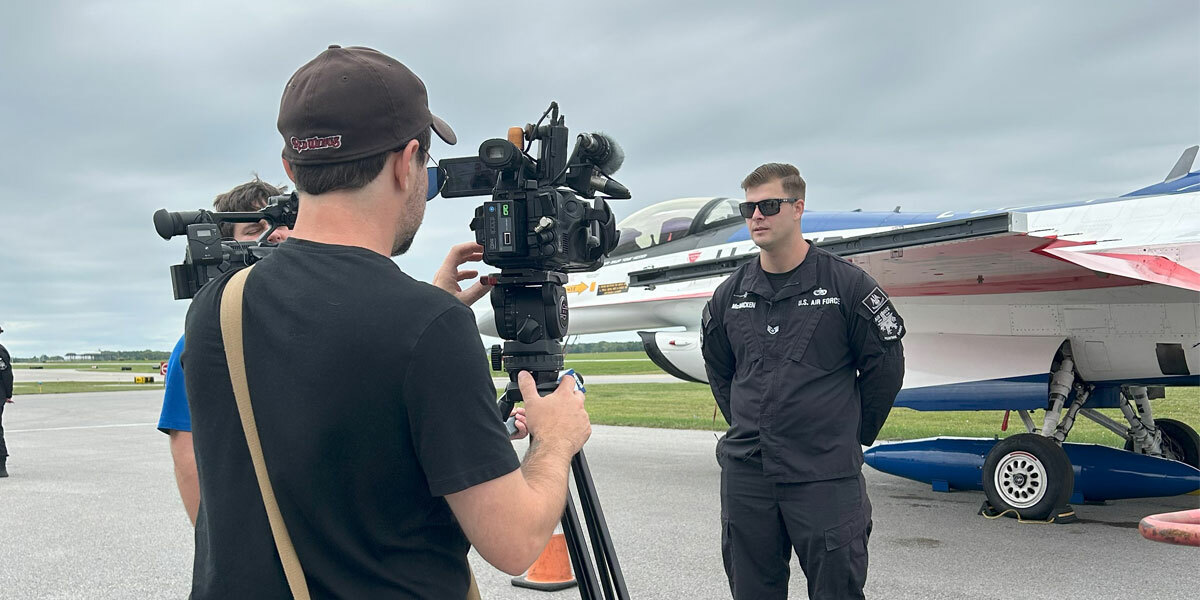 Media Crendentials - Two men standing on runway conduting interview.