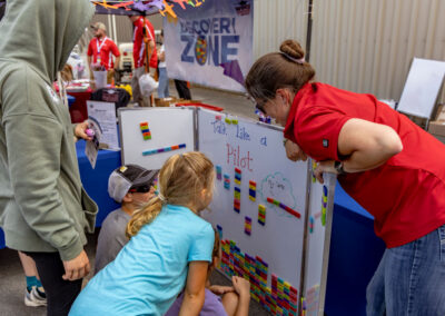 A volunteer helps children arrange colorful word magnets on a “Talk Like a Pilot” activity board in the Discovery Zone.